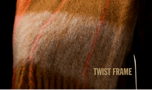 Close-up of a plaid mohair throw with 'TWIST FRAME' text on a dark background